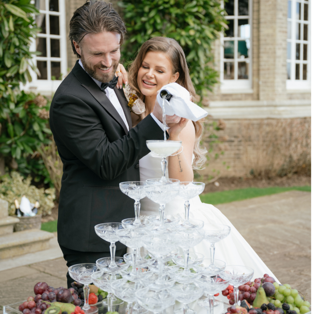 Image of a 4 tier cut glass champagne tower, surrounded at its base with a abundance of fresh fruit.